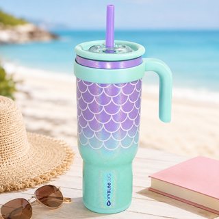 Taza marea azul VyblooJug en mesa de playa con sombrero y libro