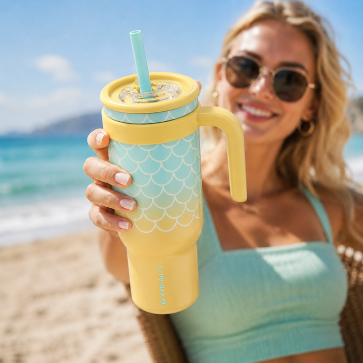 Mujer en playa sosteniendo la taza VyblooJug laguna dorada